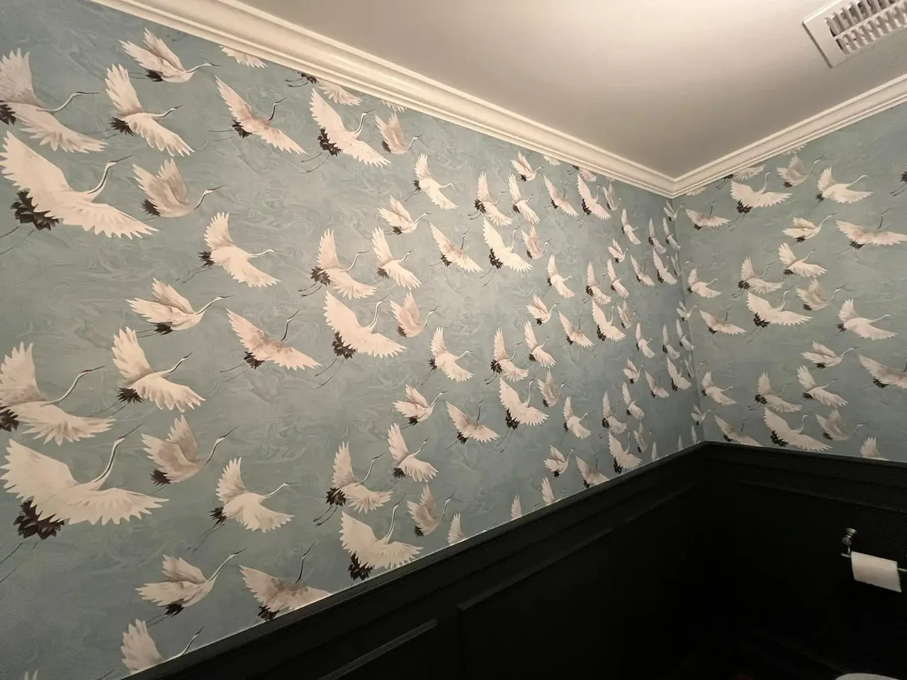 Bird-pattern wallpaper above dark paneling in a small room